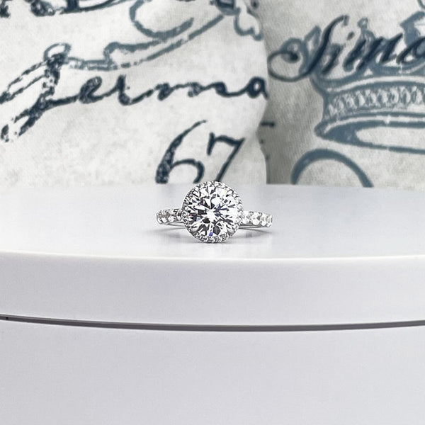 14K white gold engagement ring with 3ct round diamond, framed by a halo of smaller diamonds, on a band of pave set round cut diamonds.