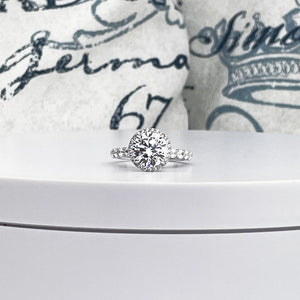 14K white gold engagement ring with 3ct round diamond, framed by a halo of smaller diamonds, on a band of pave set round cut diamonds.