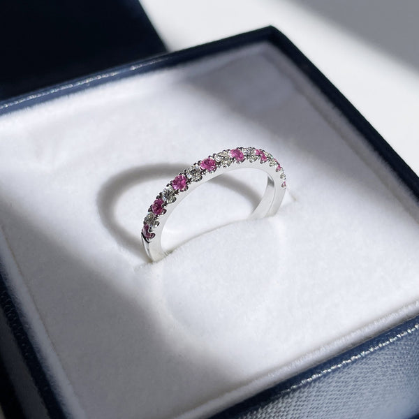 Expertly pave set pink sapphires and white diamonds in a white gold eternity ring or anniversary band is placed in a stylish blue and white ring box and framed by shadows with a beam of light shooting across the sapphire and diamond ring. CUsom made eternity band in Vancouver, BC at taurus and leo jewellery near Gastown.